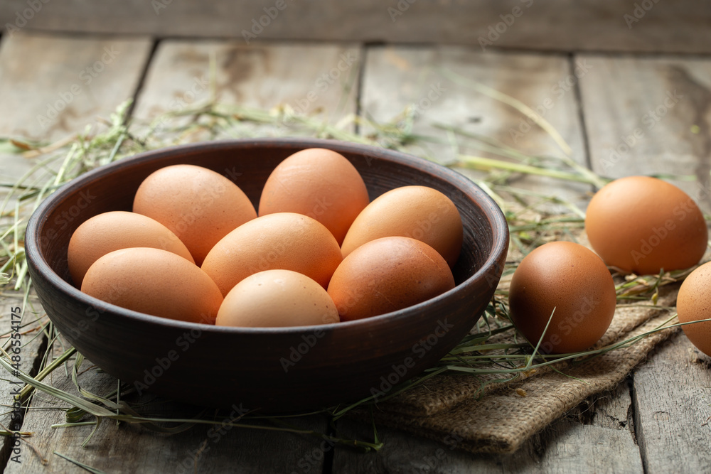 Chicken eggs in a clay bowl on a wooden background, hay scattered around. Healthy food concept. Chicken eggs in a clay bowl on a wooden background, hay scattered around. Healthy food concept.