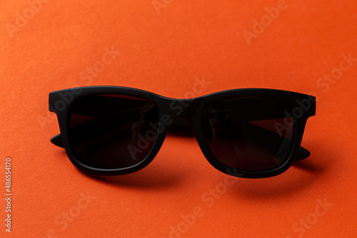 Black sunglasses on orange background  top view  flat lay  minimalistic concept of summer 