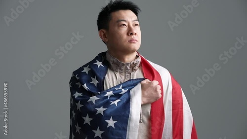 Confident soldier Asian man covered with the USA flag takes an oath in the grey studio photo