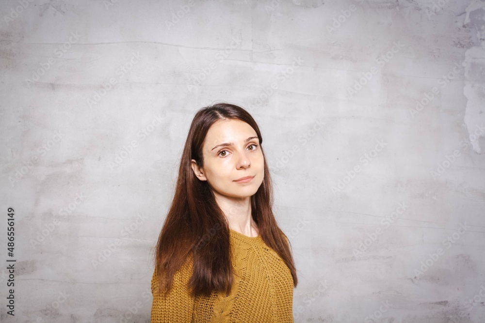 Portrait of pretty young brunette woman with long hair in amber pullover, stands in front of gray concrete background. Lifestyle fashion concept with copy space Portrait of pretty young brunette woman with long hair in amber pullover, stands in front of gray concrete background. Lifestyle fashion concept with copy space