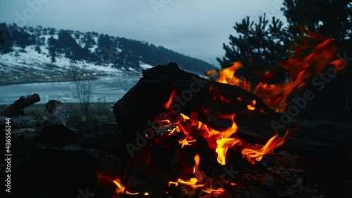 campfire burning at sunset against frozen lake view in winter camp