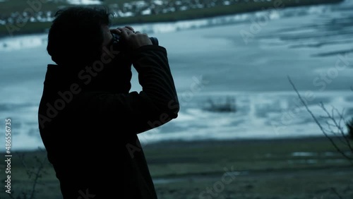 camper man watching far away with binoculars at sunset in nature in winter