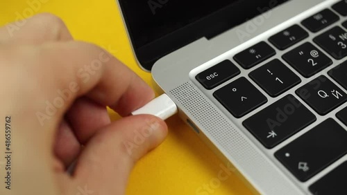 Person hand inserting a USB-C cable charger into computer or laptop for charging. Close-up view