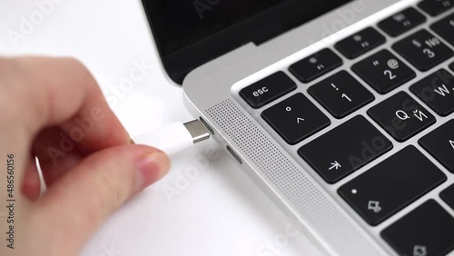 Person hand inserting a USB-C cable charger into computer or laptop for charging. Close-up view