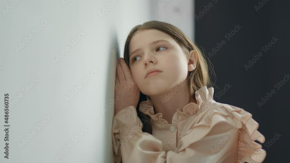 Blonde teen girl stands near a white wall and eavesdrops Blonde teen girl stands near a white wall and eavesdrops