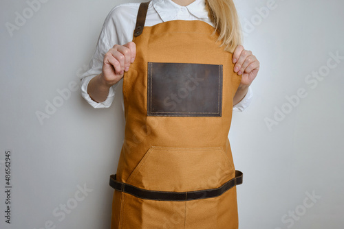 A woman in a kitchen apron. Chef work in the cuisine. Cook in uniform, protection apparel. Job in food service. Professional culinary. Camel fabric apron, casual clothing. Handsome baker posing