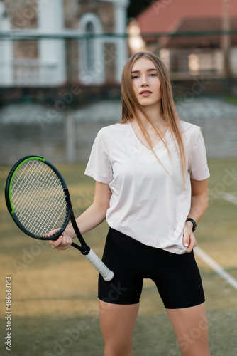 Girl athlete in a white T-shirt and black tight shorts with a racket on the tennis court. Fashion and sport concept. © Евгений Гвоздев