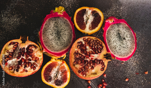 Split open dragon fruit, blood orange, and pomegranate fruit. With dark textured background. 