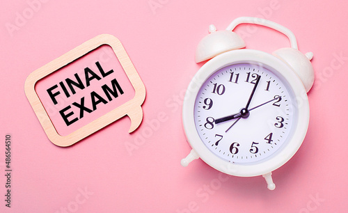 On a delicate pink background, a white alarm clock and a wooden frame with the text FINAL EXAM
