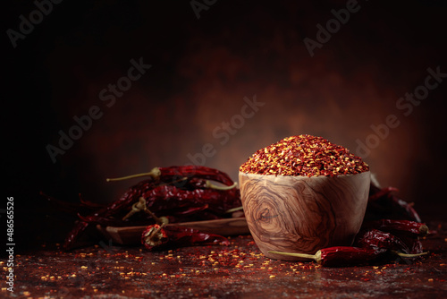 Fotografiet Chilli flakes and dried chili peppers on a brown background.
