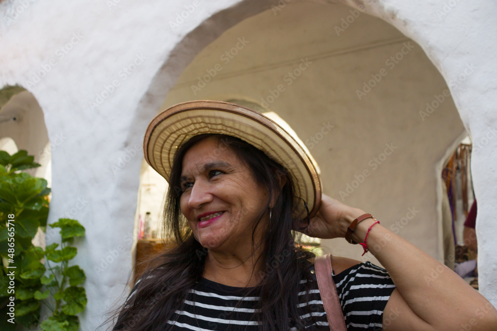 mujer adulta latina sonriente cabello largo y negro con sombrero en una plaza con fondo blanco