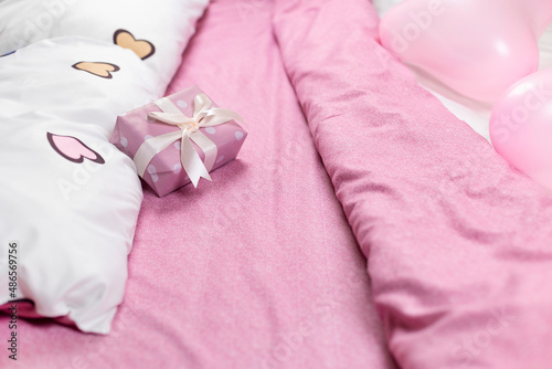 A pink gift box tied with a satin ribbon lies on pink bed linen. The concept of Valentine's Day. Selective focus.