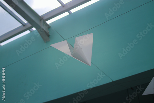 White paper plane is hanging on the ceiling with tosca wall. Childhood, dream catcher, and imagination concept