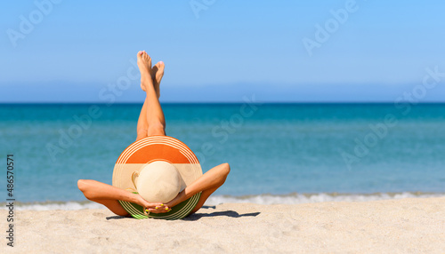 Fototapeta Naklejka Na Ścianę i Meble -  A slender tanned girl on the beach in a straw hat in the colors of the flag of India. The concept of a perfect vacation in a resort in the India. Focus on the hat.