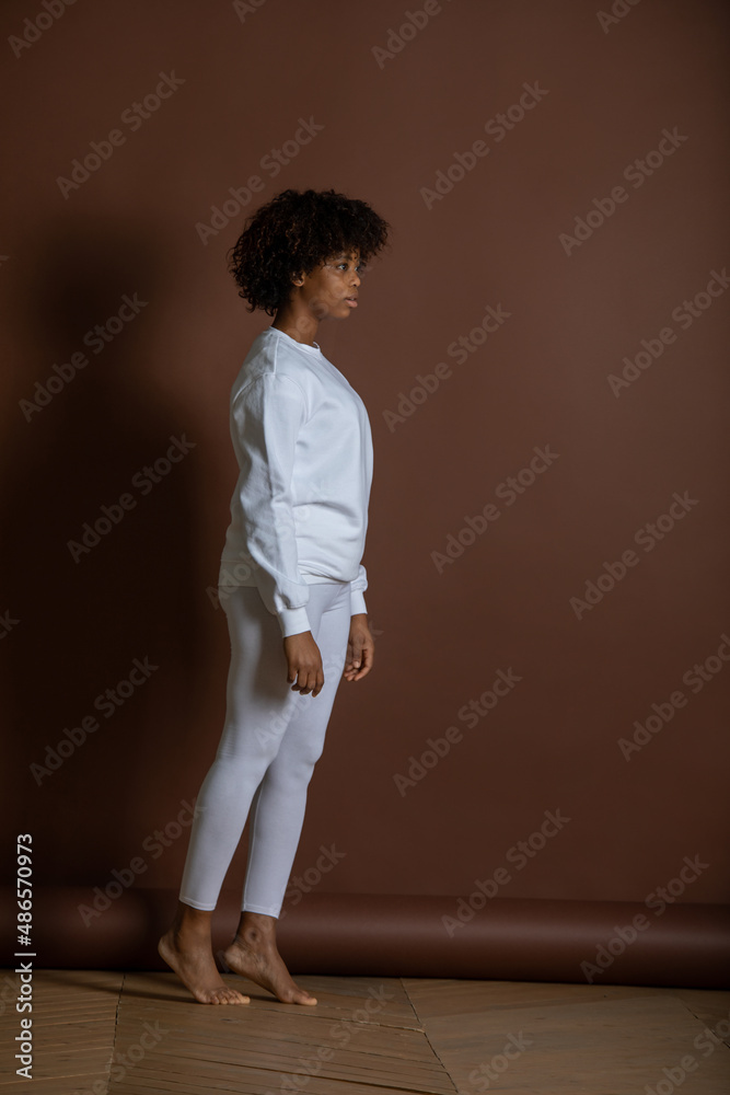 African-American girl in a white sweatshirt and leggings stands on a brown background. Mock-up.