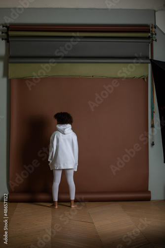 African american woman in a white hoodie and leggings stands on a brown background. Back view.