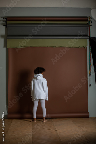 African american woman in a white hoodie and leggings stands on a brown background. Back view. © kanashkin