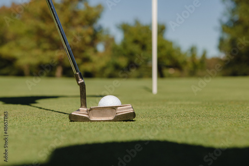 Detail of golf club about to hit the ball on the green