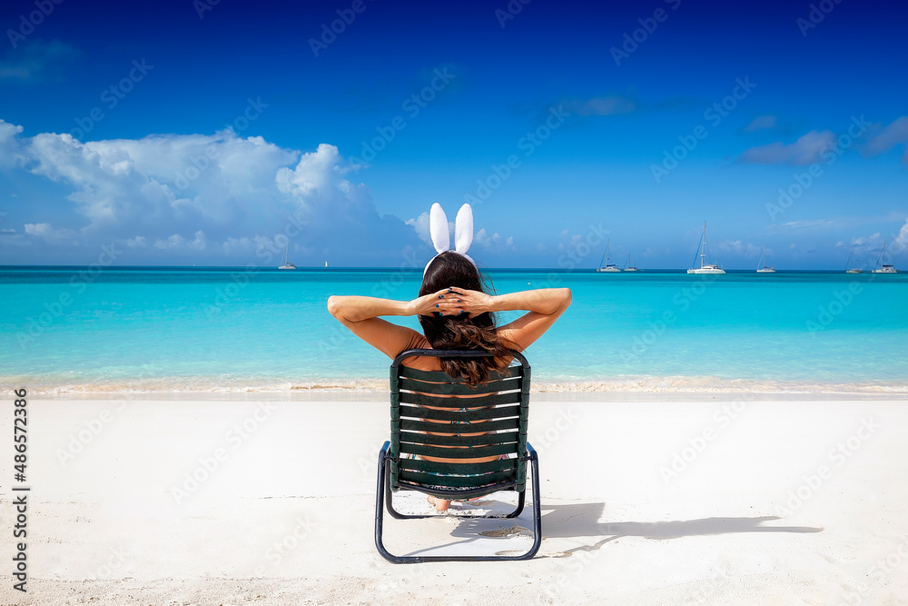A woman with easter bunny ears relaxes on a sunchair at a tropical paradise beach