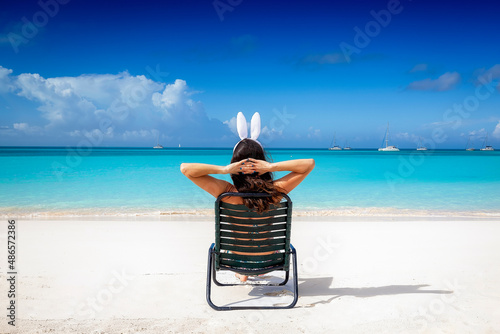 Obraz na płótnie A woman with easter bunny ears relaxes on a sunchair at a tropical paradise beach w salonie