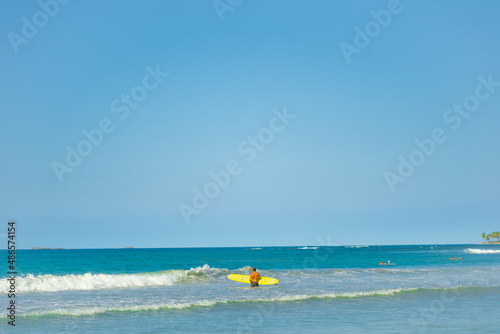 Surfing on the waves of the Indian Ocean off the tropical coast. Yellow surfboard against the blue sea. Bright blue sky over the ocean. Sunny summer day.