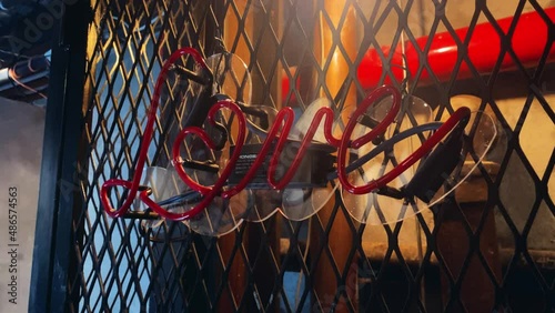 Red neon love sign flickering out with a metal fence and pipes in the background (ID: 486574563)