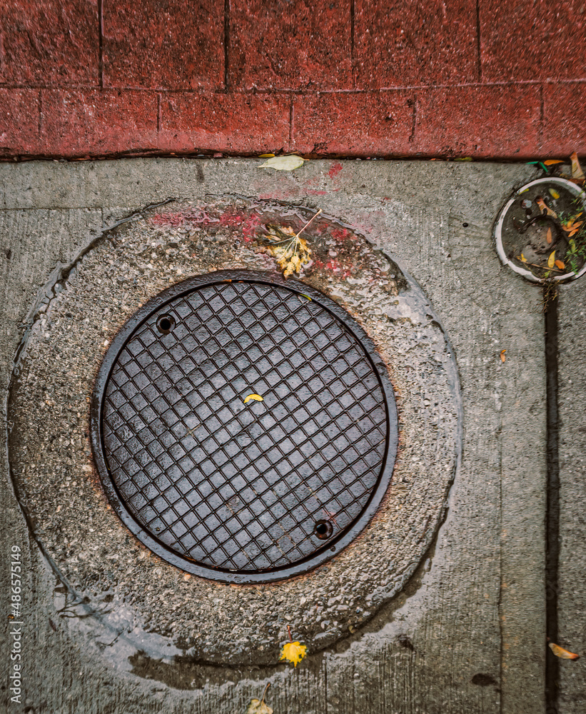 Wet metal manhole cover sits in a concrete ring with red brick paving stones along the top Wet metal manhole cover sits in a concrete ring with red brick paving stones along the top