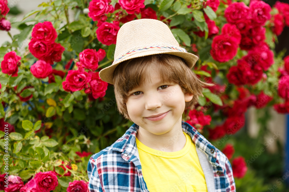 Portrait of a boy with long hair against a background of a blooming rose. Child in the summer garden. Spring kid.