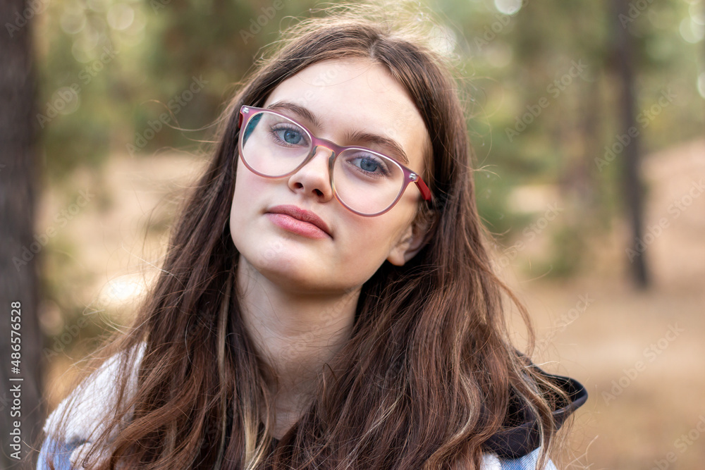 Close-up portrait of a beautiful girl in glasses on a blurred green background. Hipster teenager in the park