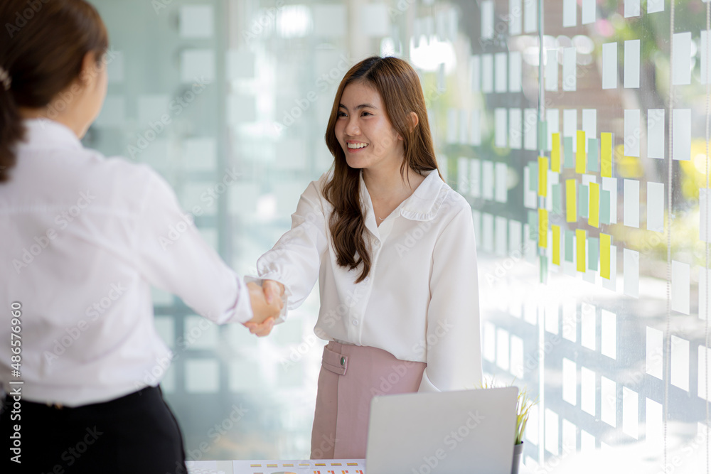 Two women shake hands, two businesswomen shake hands as they meet to discuss brainstorming and marketing plans to find more profitable ways to grow. Business management ideas for profitable growth.