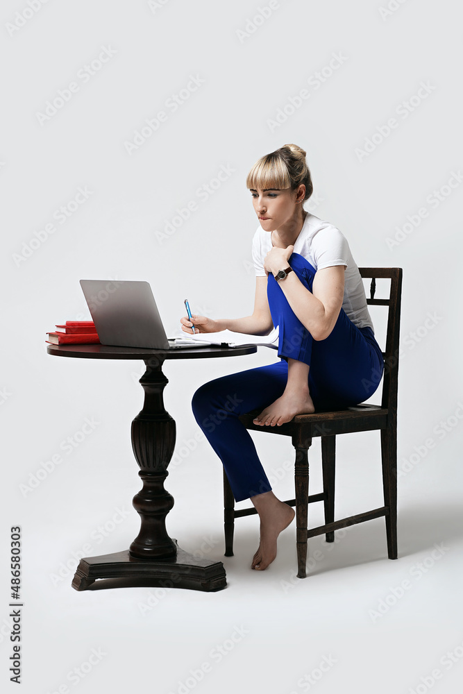 Focused young female student bites her lip while sitting at desk working or studying remotely online. Distant learning or remote work from home. Isolated on white background.