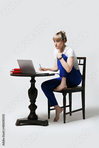 Obraz na płótnie Focused young female student bites her lip while sitting at desk working or studying remotely online. Distant learning or remote work from home. Isolated on white background. w salonie