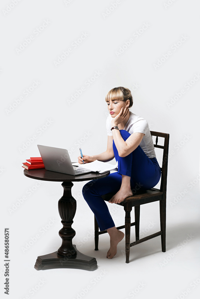 Focused young female student sitting at desk working or studying remotely online writing notes while looking on laptop screen. Distant learning or remote work from home. Isolated on white background.