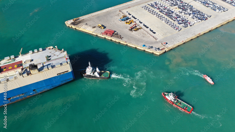 Aerial drone photo of large car carrier ro ro vessel guided by tug boats to anchor to Mediterranean car terminal port