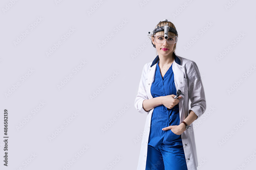 Confident ENT doctor wearing surgical headlight head light and protective glasses. Portrait of female otolaryngologist or head and neck surgeon on light grey background. Confident ENT doctor wearing surgical headlight head light and protective glasses. Portrait of female otolaryngologist or head and neck surgeon on light grey background.