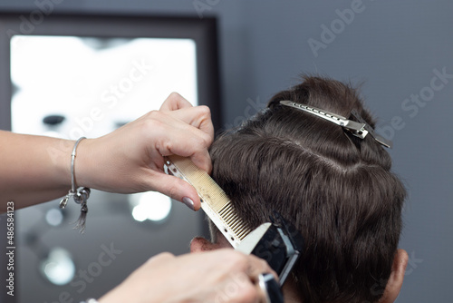 Hairdresser uses hair clipper for fringing hair, for young boy, horizontal