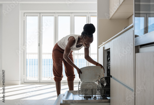 Black woman putting dirty plate into dishwasher photo
