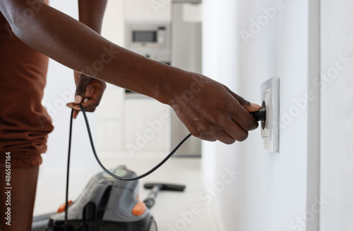 Crop black woman plugging vacuum cleaner into socket photo