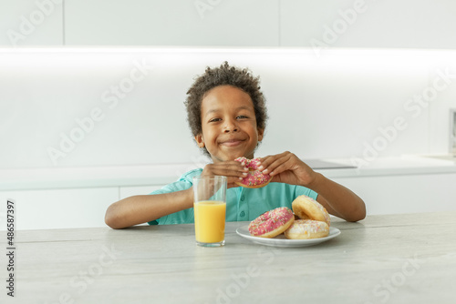 Portrait of happy child boy drinking orange juice and eating donuts