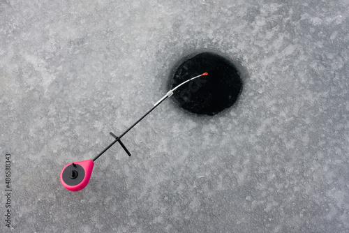 Winter ice fishing. Fishing rod is on ice near hole. Balalaika rod is popular type of rod for ice-fishing on Mormyshka. Top view. photo
