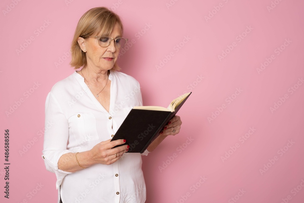 Senior smiling caucasian woman holding a book over isolated pink background. Literature concept. Senior smiling caucasian woman holding a book over isolated pink background. Literature concept.