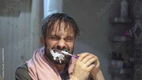 A man in the bathroom in front of the mirror furiously brushes his teeth with a toothbrush like crazy