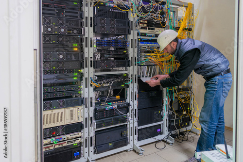 A technician works in a server room. Support for the network information infrastructure of the data center. Man connecting server with fiber optic cable