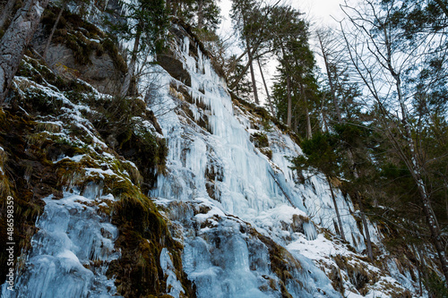 Winter landscape of a frozen waterfall falling in the forest.