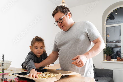 Cropped view of unrecognizable man and his daughter making sweets with biscuit cutters on processing board. Father putting cookies on the baking sheet
