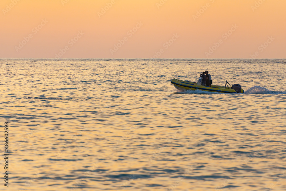 Motor boat at sea. A yellow rubber boat cleaves the calm sea in the sunset light.
