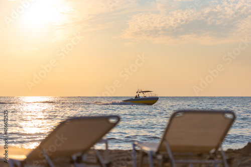 The backs of the sun loungers in front of the sea with a boat. Evening on the beach. Focus on the boat. © Михаил Шаповалов