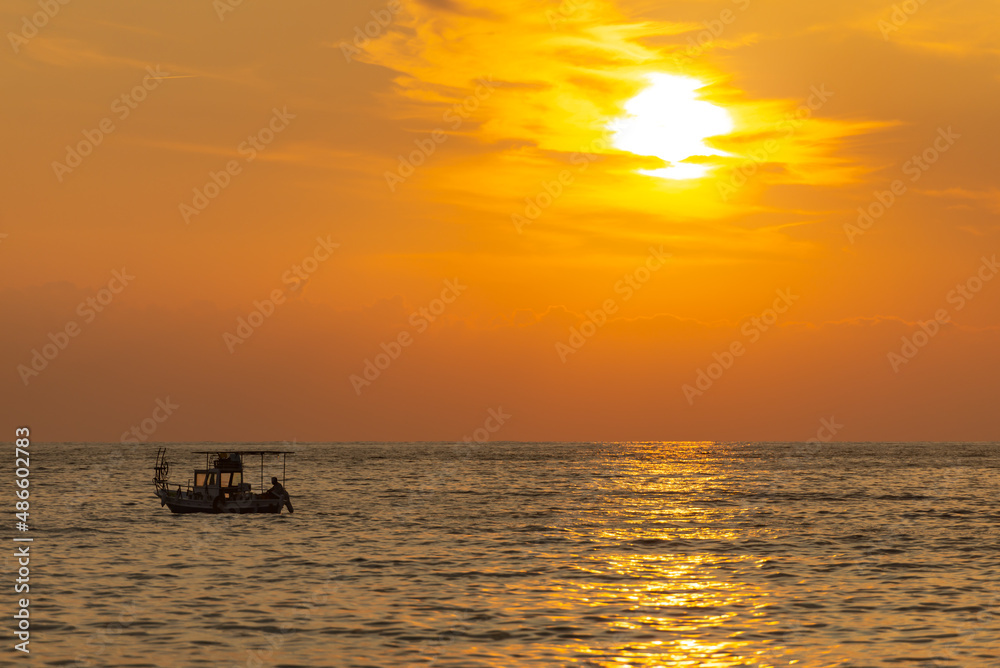 A fishing boat goes out to sea at sunset. A sunny path on the sea and a dark boat on its background.