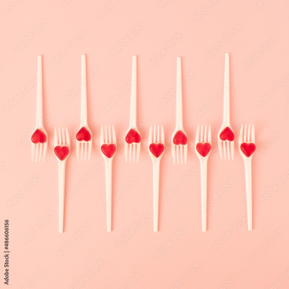 Creative arrangement made of white forks with red candy hearts on pastel pink background. Minimal Valentines day or wedding layout. Flat lay. Creative arrangement made of white forks with red candy hearts on pastel pink background. Minimal Valentines day or wedding layout. Flat lay.