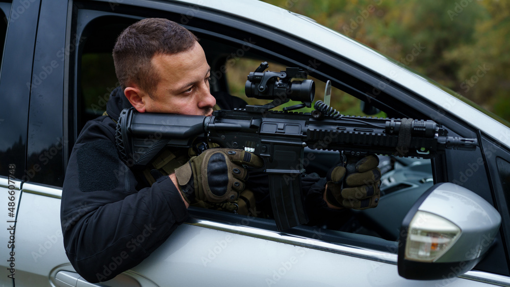 One man special force police or terrorist holding automatic weapon shooting and aiming from the car anti-terrorist unit on the mission under attack in vehicle copy space side view One man special force police or terrorist holding automatic weapon shooting and aiming from the car anti-terrorist unit on the mission under attack in vehicle copy space side view